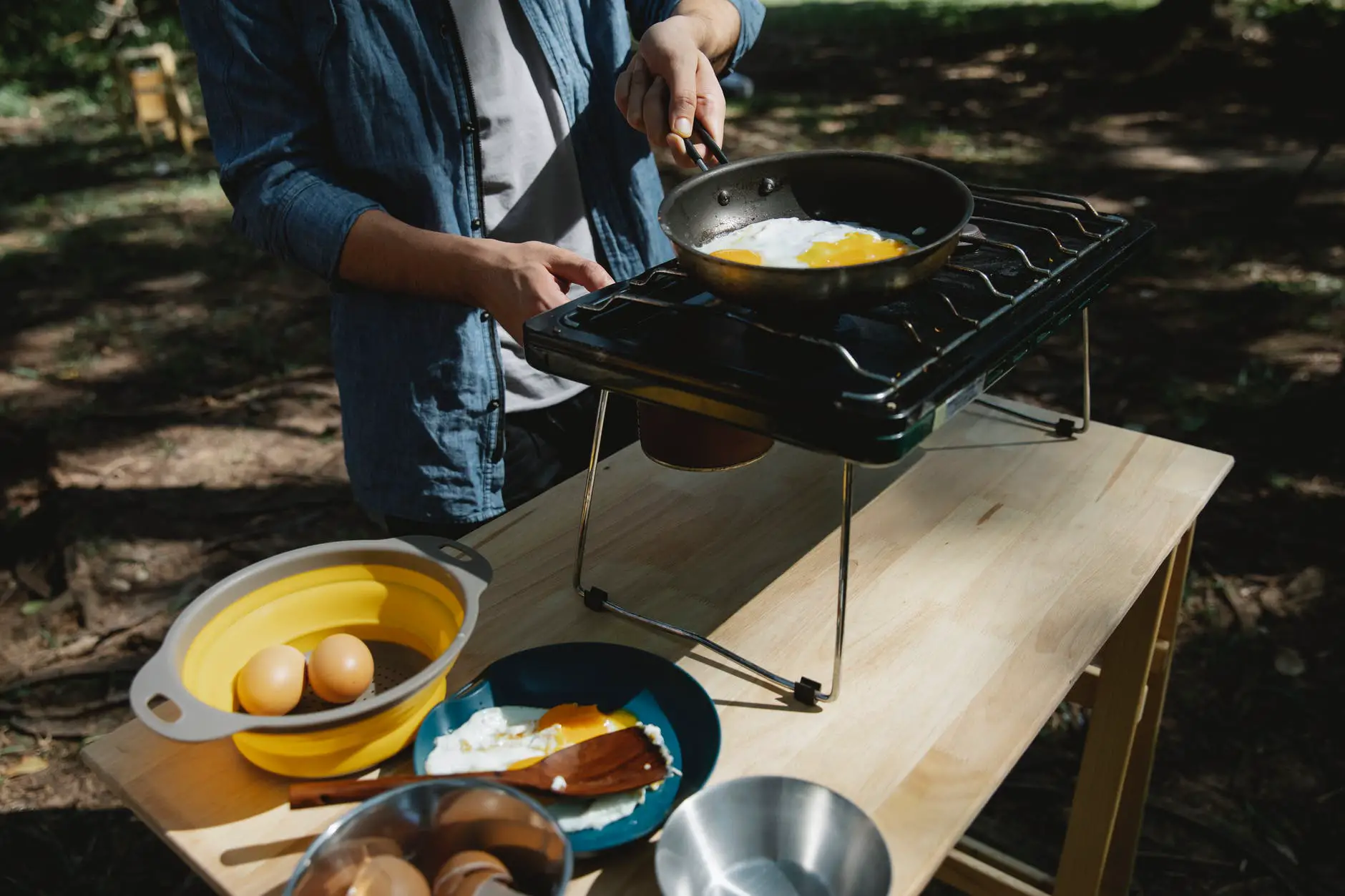 unrecognizable man frying eggs in camping