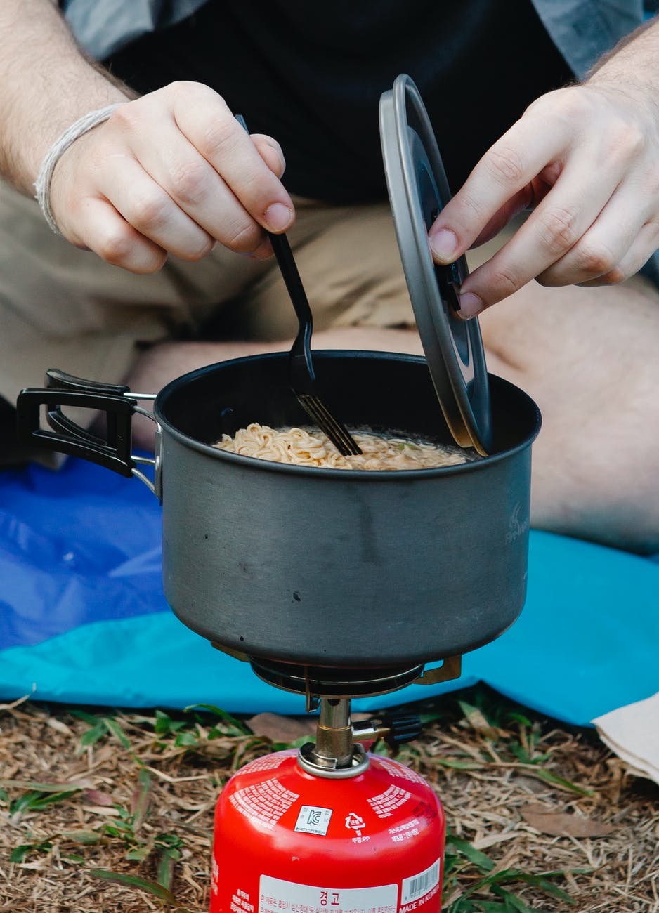 anonymous man cooking on camping stove after hiking in forest