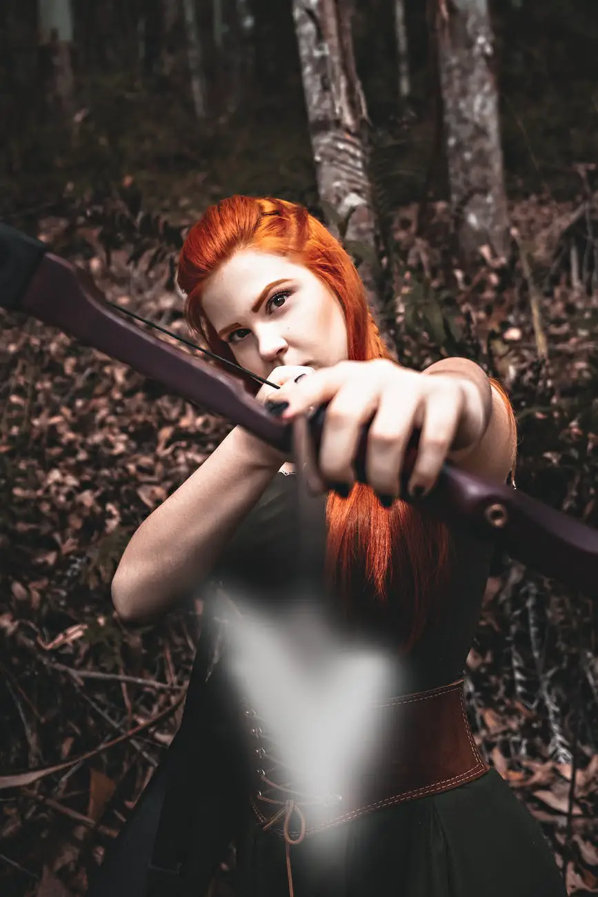 serious redhead female archer in medieval costume hunting with bow in forest