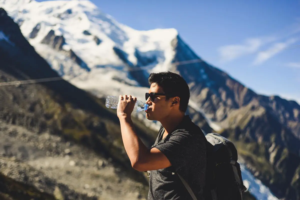 A person drinking water from a reusable bottle while hiking in the mountains. fall camping essentials